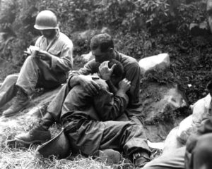 A grief stricken American infantryman whose buddy has been killed in action is comforted by another soldier. In the background a corpsman methodically fills out casualty tags, Haktong-ni area, Korea. August 28, 1950. Sfc. Al Chang. (Army) NARA FILE # 080-SC-347803 WAR & CONFLICT BOOK #: 1459