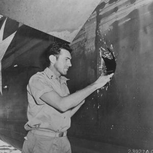 1Lt Louis Zamperini, bombardier of this B-24D Liberator 'Superman' peering through a hole in the aircraft from a 20mm shell over Nauru, Apr 20 1943; photo taken at Funafuti, Gilbert Islands. Source: National Archives